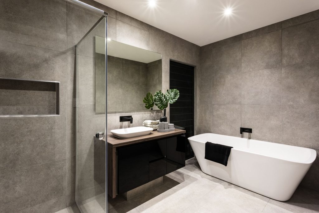 Modern bathroom with a shower area and freestanding bathtub including a wall mirror beside a fancy plant near a tap and sink over the wooden counter and dark cupboard