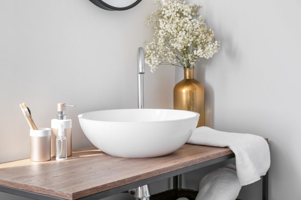 Luxurious white bathroom sink with wooden countertop and copper vase with flowers