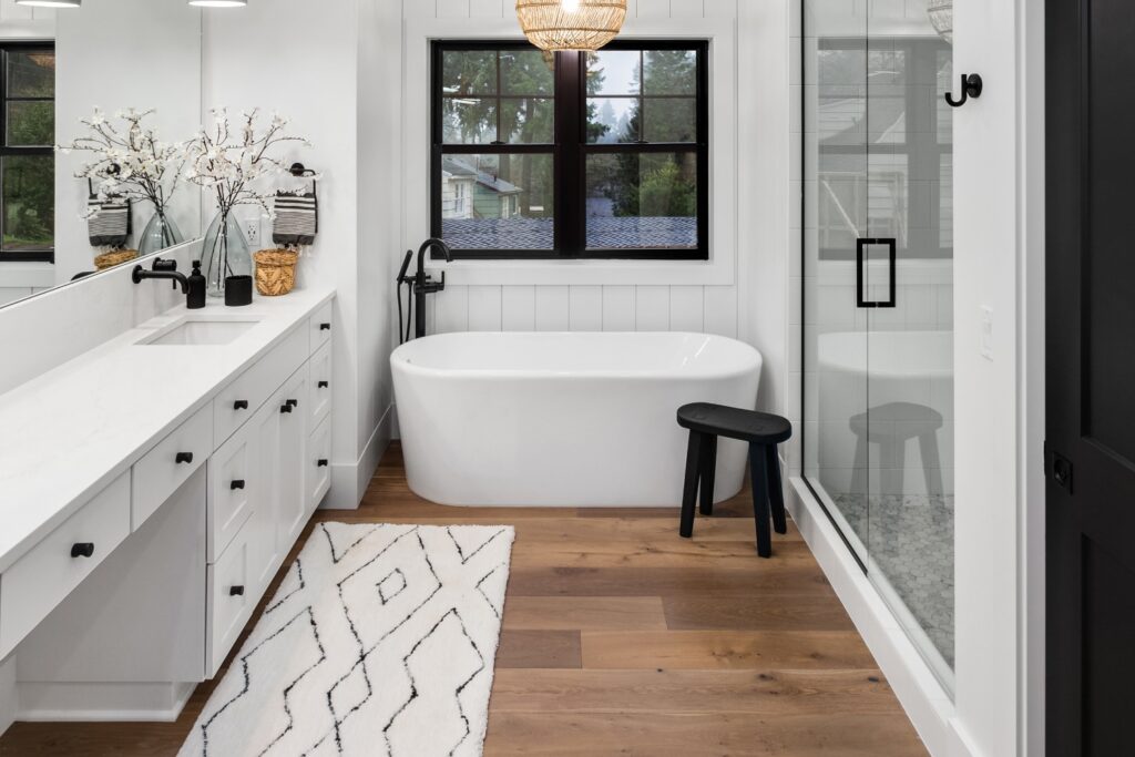 Beautiful bathroom in luxury home with double vanity, bathtub, mirror, sinks, shower, and hardwood floo